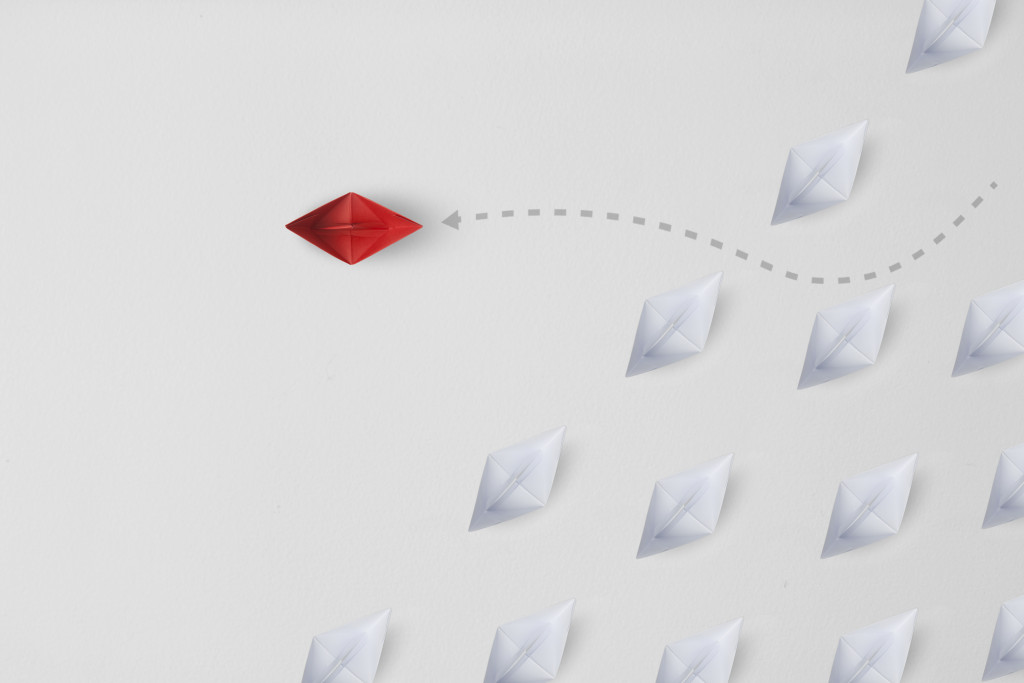 a lone red paper boat sailing off from a crowd of white paper boats, representing uniqueness